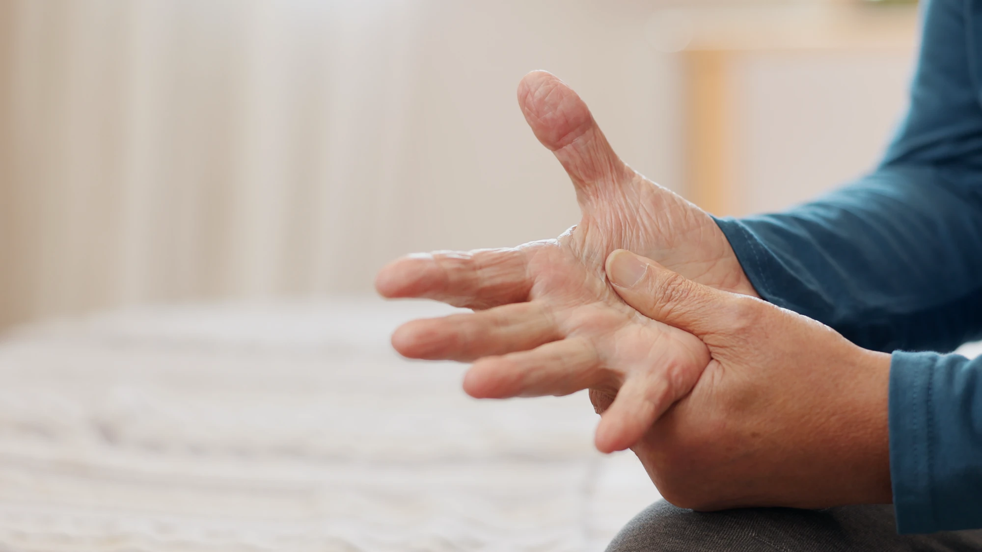 A close-up of an elderly person's hands. One hand grips the palm of the other, suggesting joint discomfort or the massaging of pain.