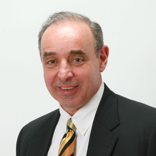 A professional headshot of Dr. Moramarco smiling, wearing a dark suit, white shirt, and a striped gold and black tie against a light background.