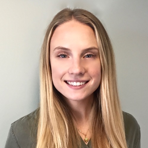 Kim Kruzel, a woman with long blonde hair, smiles widely in a professional portrait while wearing an olive shirt and a gold necklace.